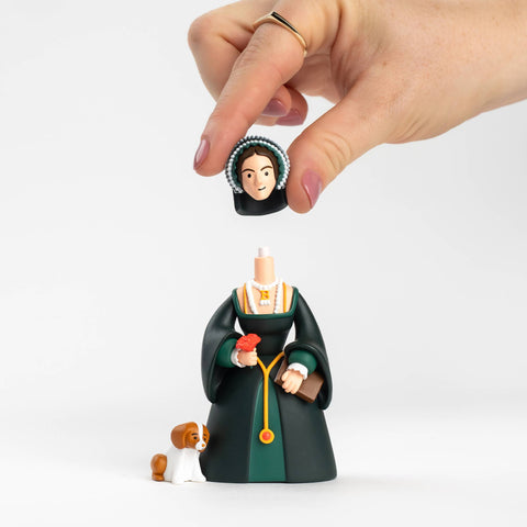 Hand holding a figurine of Anne Boleyn in a green dress with a dog, on a white background