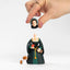 Hand holding a figurine of Anne Boleyn in a green dress with a dog, on a white background